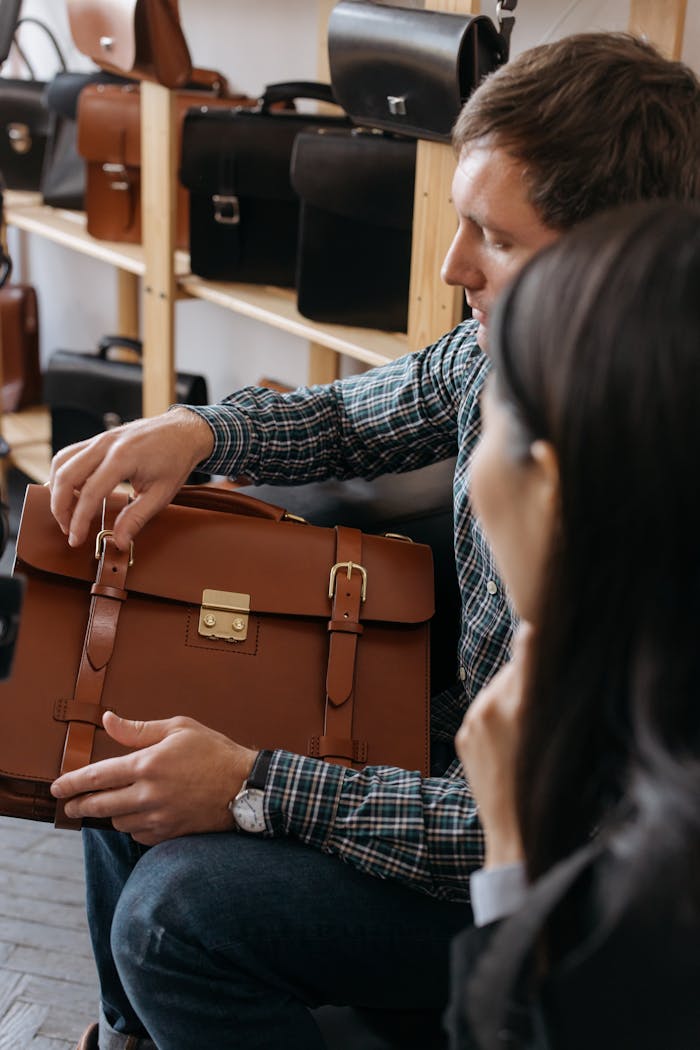 about-us-01 A man sits indoors examining a stylish leather briefcase in a store setting.